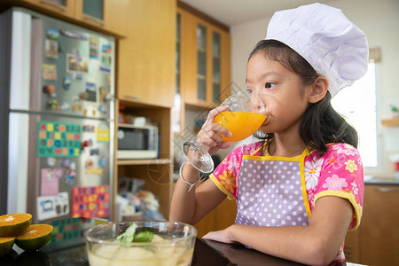 穿着厨师服的小女孩在厨房喝橙汁图片