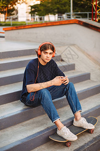 戴着橙色耳机的年轻溜冰者手里拿着手机图片