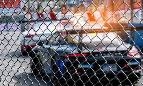在柏油路上赛车从赛马场背景上模糊的汽车上的栅栏网看街道赛上的超级赛车图片