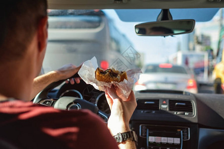 男人在吃汉堡时驾驶汽车等待和站图片