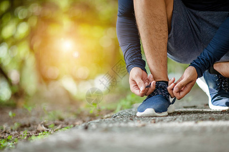 男子系慢跑鞋一个人在阳光明媚的日子在户外跑步关注两只手伸向鞋的侧面年轻的男慢跑员在户背景图片