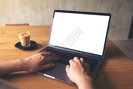 一名使用笔记本电脑空白桌面屏幕和木桌咖啡杯的妇图片