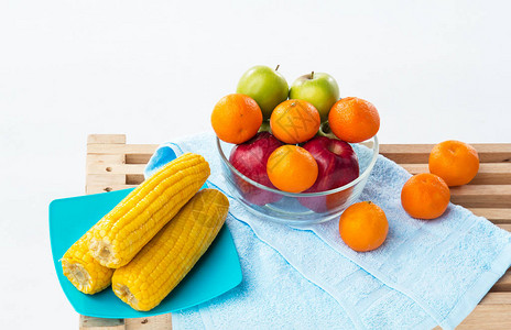 红苹果青苹果和橙子的果盘放在黄玉米盘旁边图片