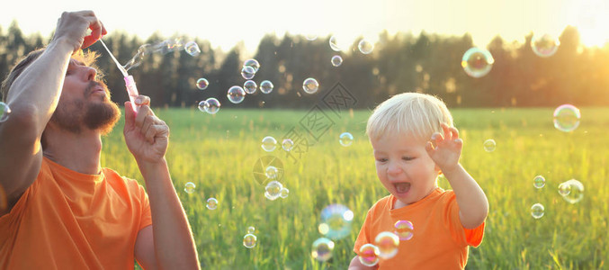 可爱的小孩金发男孩和父亲在夏日田玩肥皂泡图片