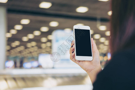 一名妇女在机场站着等待行李领取时手持和使用带有空白黑屏的白色手图片