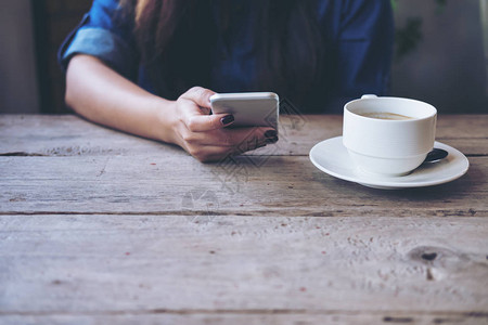 一个拿着和使用智能手机的女人坐在老式咖啡馆里图片