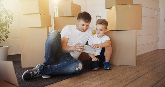 搬家日在新房子里有纸板箱的家庭父亲和孩子在新房子里父亲和儿子坐着使用图片