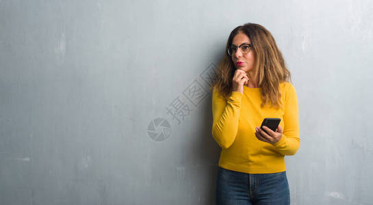 中年的希帕尼女人使用智能手机严肃的面孔思考问题图片