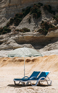 两张蓝色的甲板椅子和一张沙滩伞还有绿色条纹在马耳他一个图片