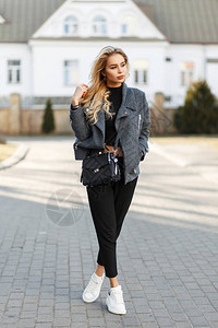 美丽的年轻时尚女孩穿着时装灰色大衣黑裤子和白运动鞋的袋子在阳光明媚图片