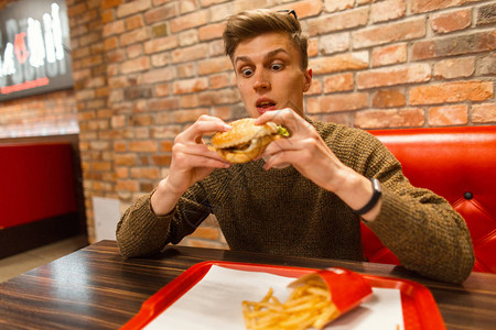 英俊的年轻人吃一个美味的汉堡包餐图片