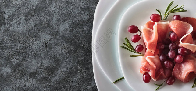 在白色盘子上配有迷迭香和葡萄的Prosciutto服务顶端视图图片
