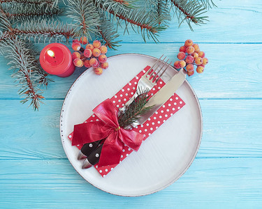 盘子叉子刀子蜡烛蓝色木质背景上的圣诞树枝图片