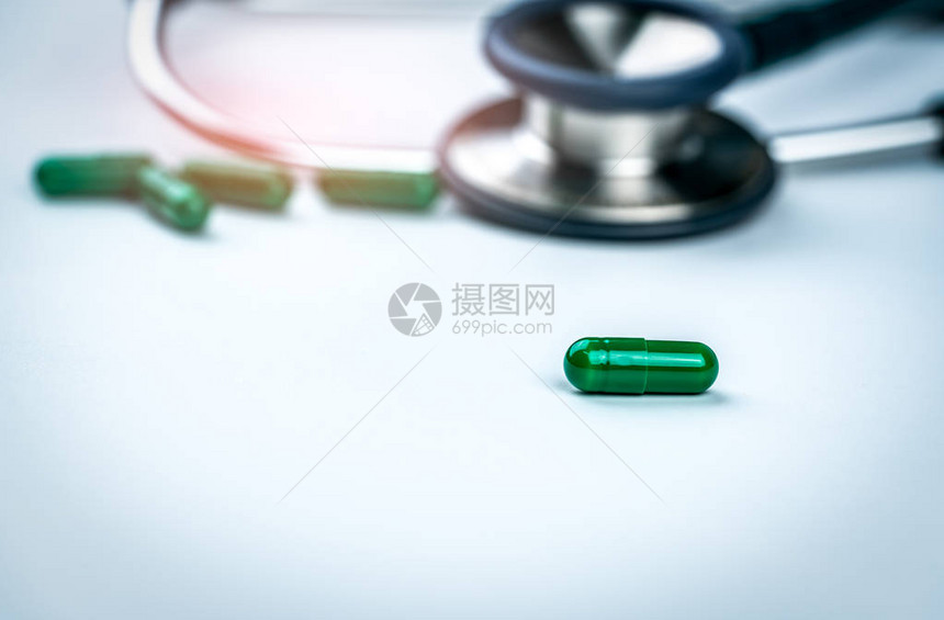 在听诊器模糊和绿色胶囊医学背景下选择地关注绿色胶囊丸医生白桌上的药物和听诊器医疗保健和康检查的概图片