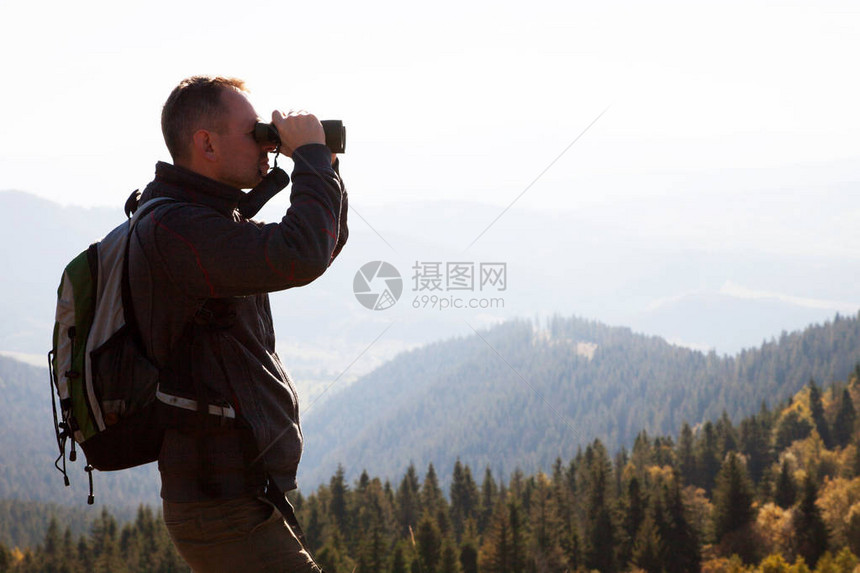 一个年轻人站在山丘上望着远处的双筒图片