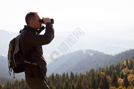 一个年轻人站在山丘上望着远处的双筒图片