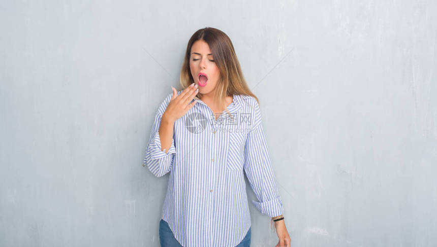 穿着时尚商务装的灰色垃圾墙上的年轻成年女无聊地打着哈欠累了用手捂住嘴图片