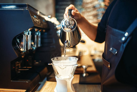 男咖啡师用咖啡咖啡柜台和咖啡机将热水倒入玻璃杯中图片
