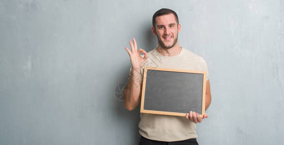 年轻的天主教男子在灰色的黑板墙壁上拿着黑板用手指做好标记图片