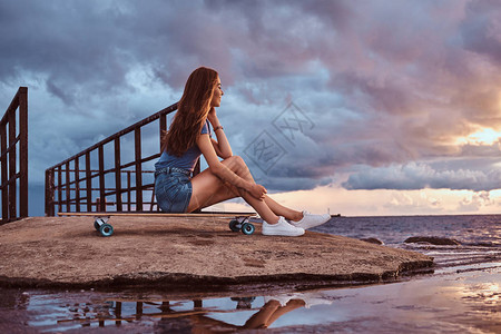 坐在海滩滑板上的感女孩的肖像在日落时正在享受令人惊叹的图片