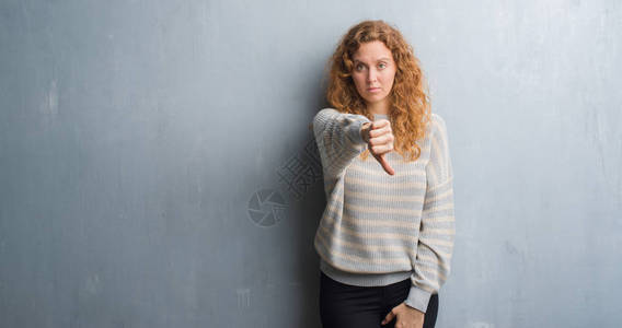 年轻红发女人在灰色的墙壁上看着不开心和愤怒图片