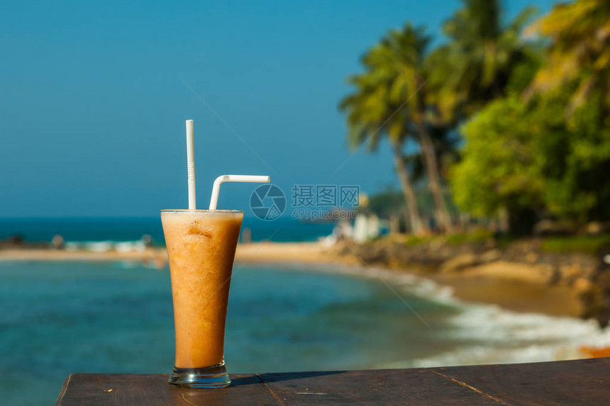 以大海和棕榈树为背景的新鲜果汁玻璃杯图片