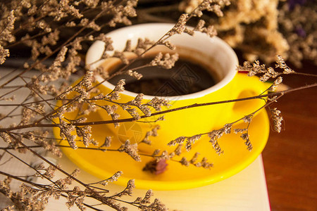 黄色陶瓷咖啡杯的深色光线设计背景放在干花信条和艺术风格的后面图片