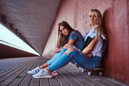 两个漂亮的时髦女孩坐在滑板上靠在图片