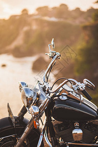 在温暖的阳光下站在悬崖边上的老式摩托车图片