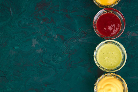 一套不同的酱汁在绿色背景的小碗里调味番茄酱芥末蛋黄酱图片