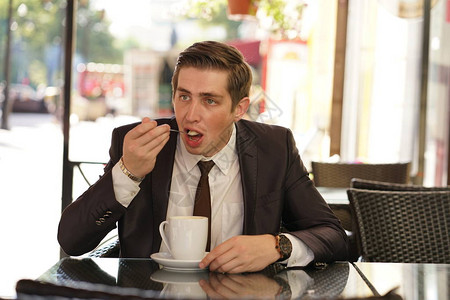 身穿黑色商业西装白衬衫和领带的年轻人坐在市郊咖啡厅的桌子上图片