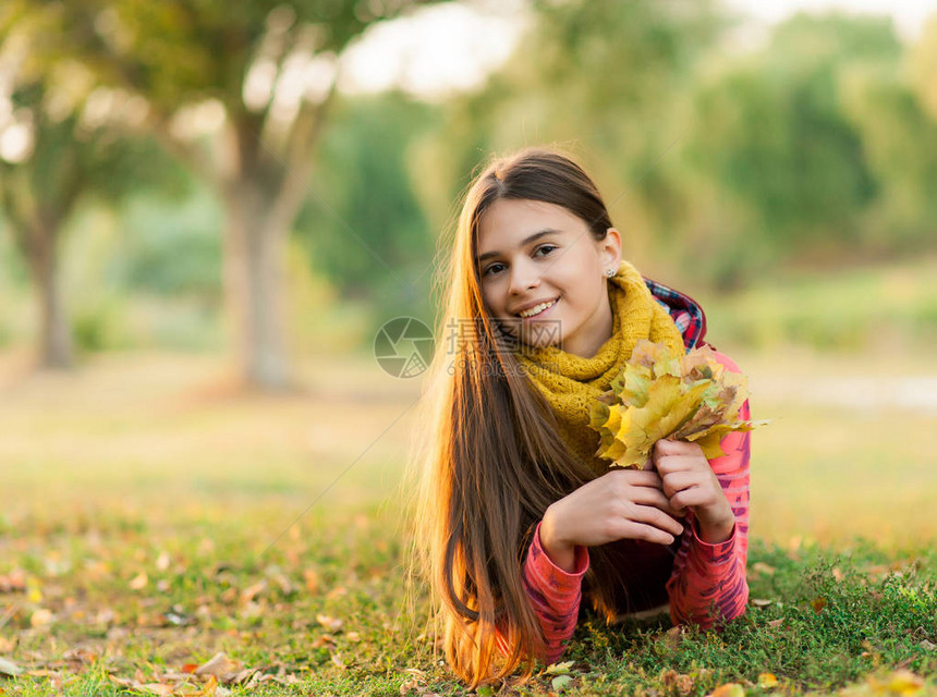 微笑着躺在秋天枫叶上的年轻女孩在户外秋天一个美丽微笑的少年的画像年轻的少女看着相机秋天图片