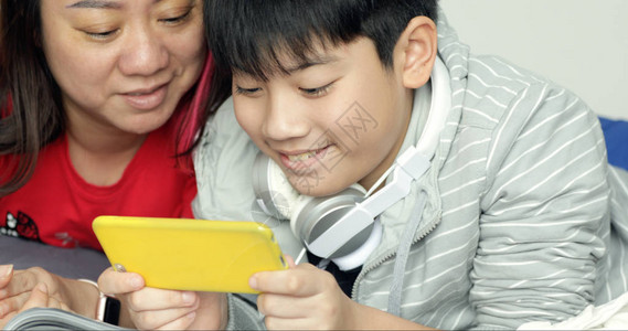 亚洲家庭的年轻母亲带着儿子在床上玩手图片