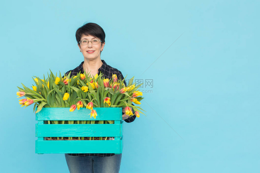 快乐的中年花店女花匠戴眼镜带着一盒蓝色图片