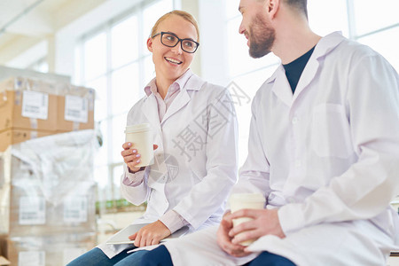 两位身穿白大褂的技术人员坐在乳品厂宽敞的包装部图片