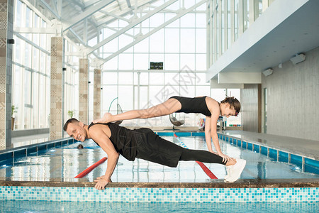 充满自信的游泳教练在游泳池边缘表演木板时与背上的女孩保持平衡图片