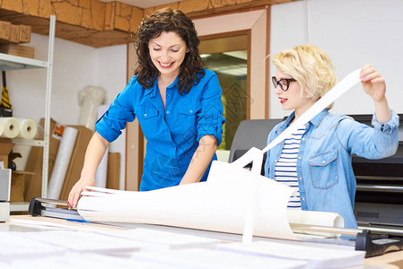 两个漂亮的女人在印刷厂工作时笑着撕开条纹的绘图纸背景图片