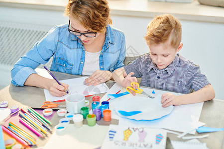 现代年轻母亲在家里艺术时间与可爱的儿子一起坐在画桌旁制作图片