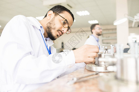 阿拉伯浓缩工程师穿着办公桌和压力传感器组装室外的实验室大衣图片