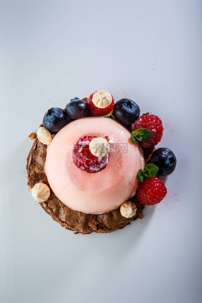 白盘上覆盖着新鲜覆盆子和蓝莓的美味粉色甜图片