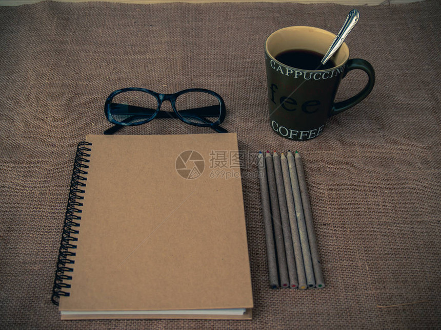 复古风格有闭合的笔记本眼镜一杯咖啡铅笔和粗麻布背景的图片