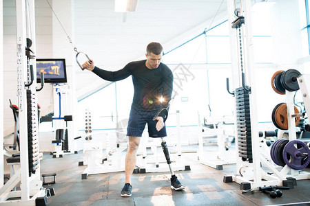 在现代健身房使用机器锻炼假腿的英俊肌图片