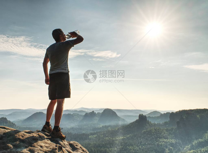 低龄男子在岩石峰顶上用塑料瓶喝水纯粹的图片