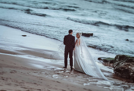 迷人的结婚情侣在夜晚的阳光下在海浪附近的沙滩上互相图片