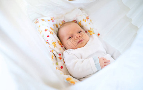 一个可爱的新生婴儿躺在床上被白毯盖着图片
