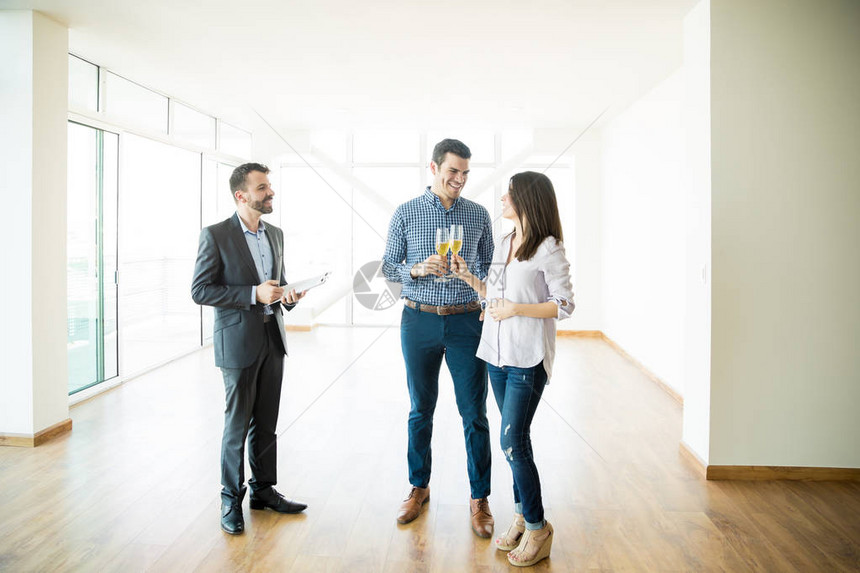 房地产经纪人看着一对夫妇在新公寓里庆祝香槟图片