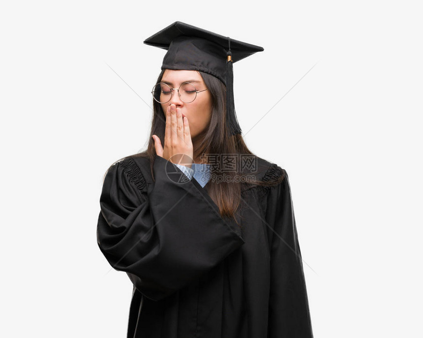 身着毕业帽子和制服的无聊打哈的年轻女用手遮住嘴唇图片