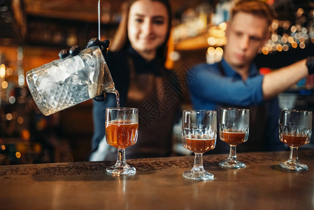 酒吧柜台的男和女调酒师酒精饮料准备工作在客图片