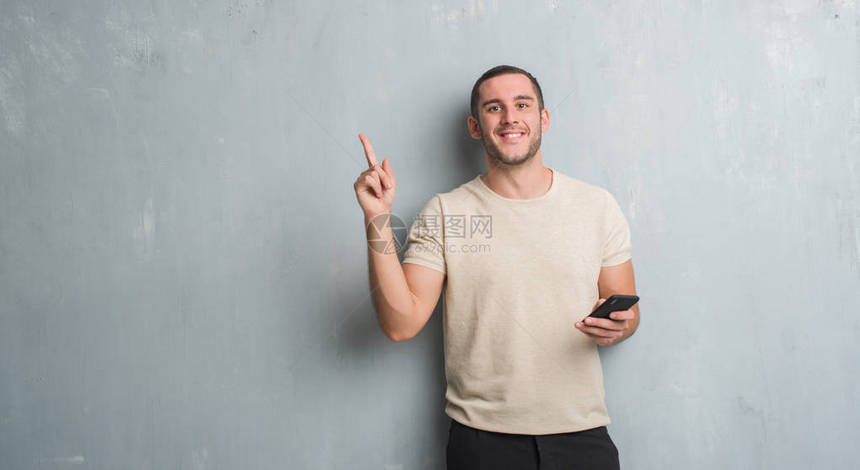 年轻的白人男子在灰色的格朗基墙上用智能手机发短信图片