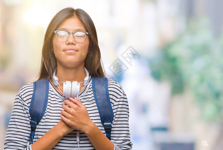 年轻女学生带着耳机和背包在孤立的背景上微笑图片